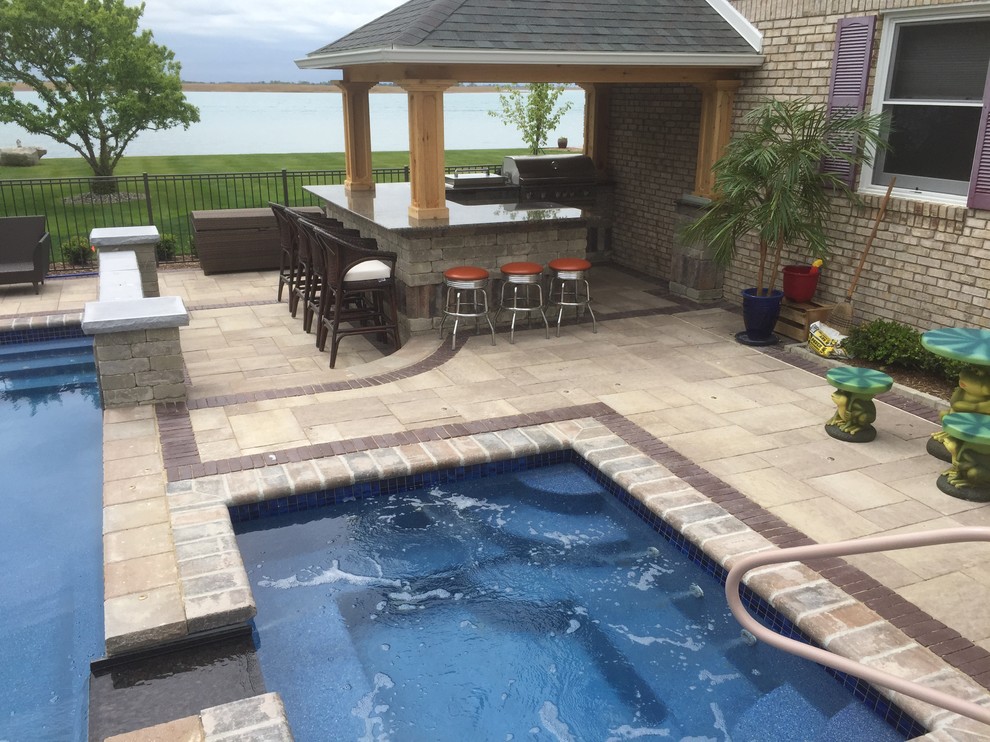 This is an example of a transitional backyard custom-shaped pool in Detroit with a hot tub and brick pavers.
