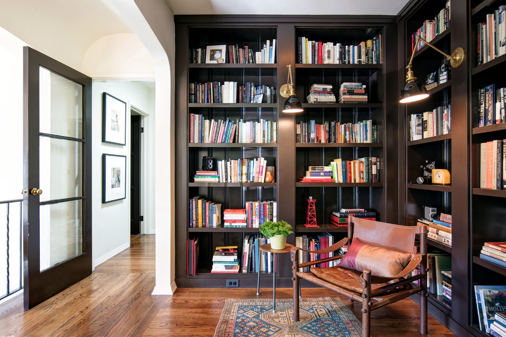 Photo of a mid-sized mediterranean home office in Los Angeles with a library, medium hardwood floors, orange floor and white walls.