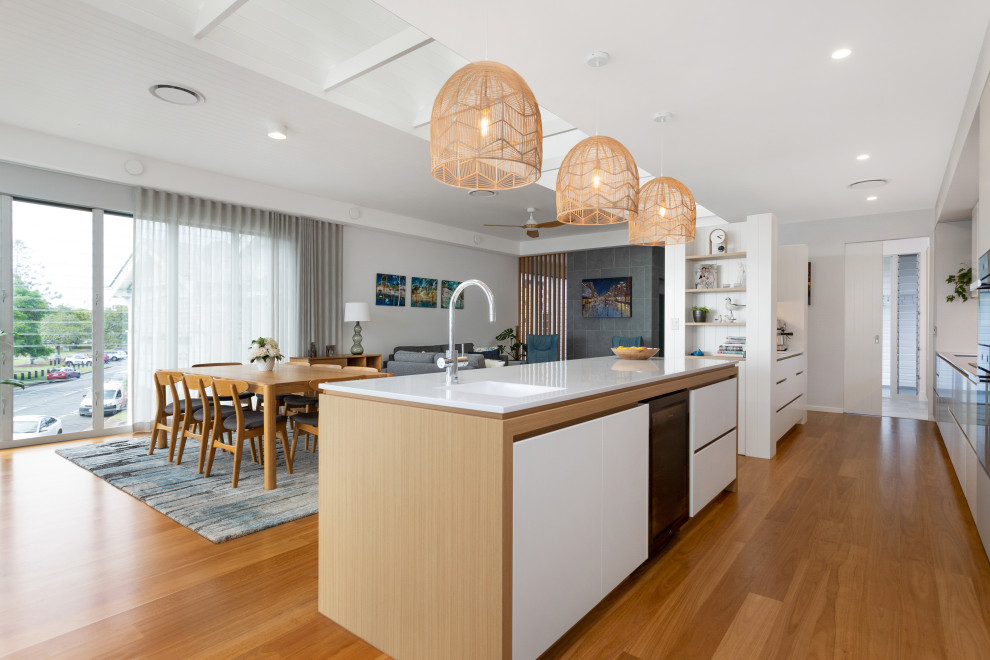 Design ideas for a large beach style galley open plan kitchen in Brisbane with an undermount sink, shaker cabinets, white cabinets, solid surface benchtops, beige splashback, marble splashback, black appliances, medium hardwood floors, multiple islands, brown floor and white benchtop.