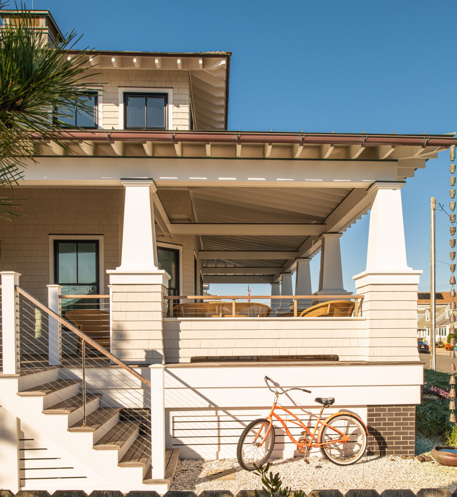 Exemple d'un grand porche d'entrée de maison avant bord de mer avec des colonnes, une terrasse en bois, une extension de toiture et un garde-corps en câble.
