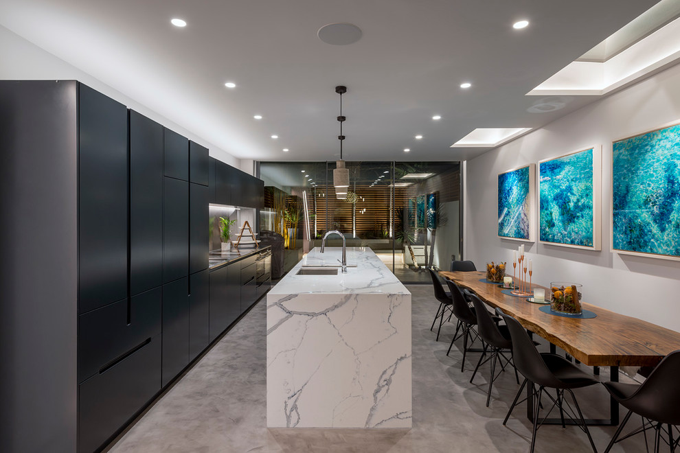 Photo of a contemporary galley eat-in kitchen in London with an undermount sink, flat-panel cabinets, black cabinets, concrete floors, with island, grey floor and white benchtop.