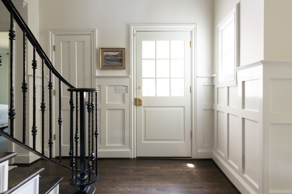 Aménagement d'un petit hall d'entrée classique avec un mur blanc, parquet foncé, une porte simple, une porte blanche, un sol marron et boiseries.