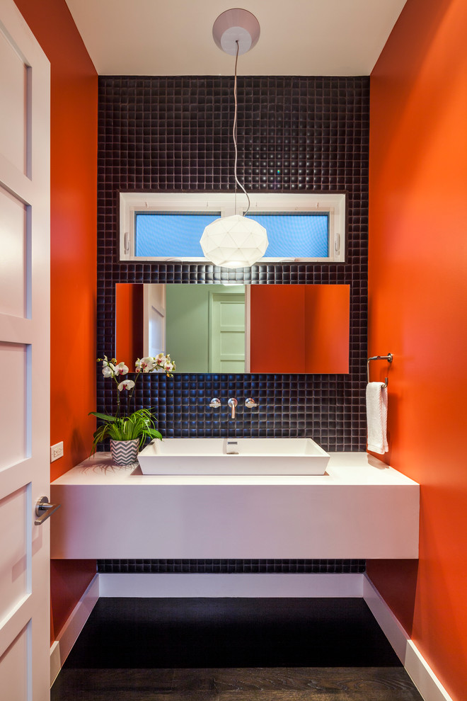 This is an example of a contemporary powder room in San Francisco with a vessel sink, black tile, a two-piece toilet, mosaic tile, orange walls and dark hardwood floors.