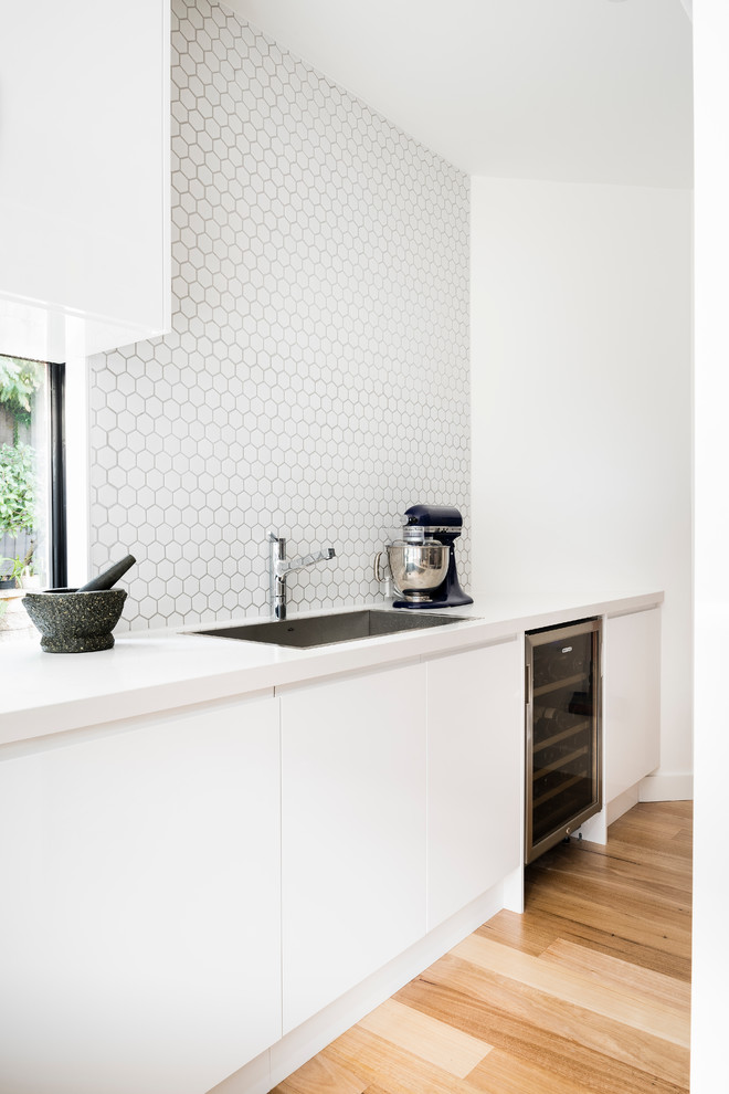 Large contemporary l-shaped kitchen pantry in Melbourne with a drop-in sink, flat-panel cabinets, white cabinets, quartz benchtops, white splashback, cement tile splashback, black appliances, medium hardwood floors and with island.