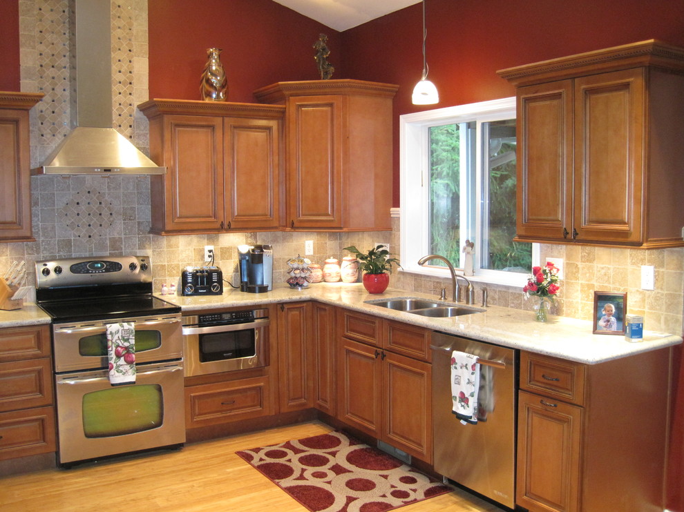 This is an example of a mid-sized traditional l-shaped eat-in kitchen in Seattle with a double-bowl sink, beaded inset cabinets, medium wood cabinets, granite benchtops, brown splashback, stone tile splashback, stainless steel appliances, light hardwood floors, no island and beige floor.