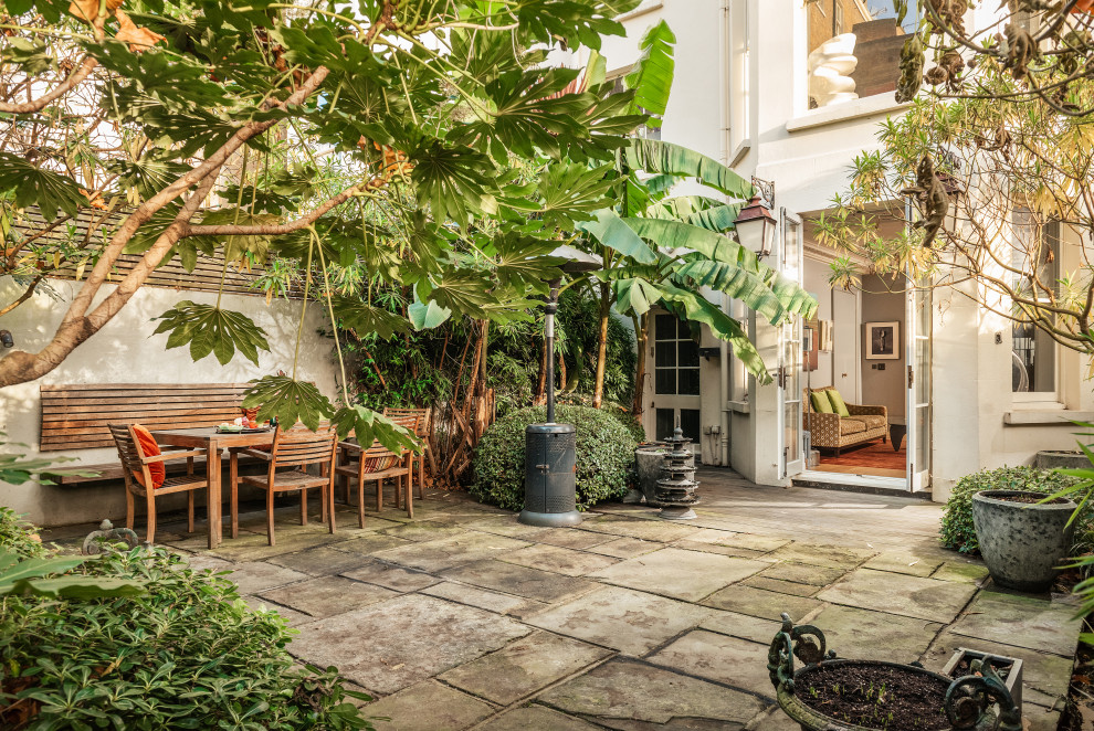 Medium sized eclectic back patio in London with natural stone paving.