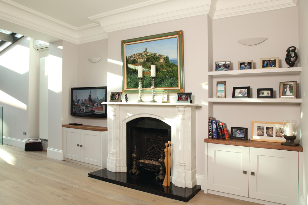 This is an example of a large transitional formal open concept living room in London with pink walls, light hardwood floors, a standard fireplace, a stone fireplace surround and a wall-mounted tv.