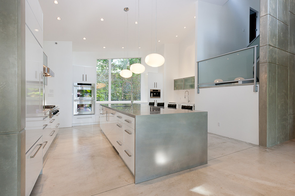 Photo of a large modern l-shaped eat-in kitchen in Vancouver with a drop-in sink, flat-panel cabinets, white cabinets, granite benchtops, white splashback, stainless steel appliances, concrete floors and with island.