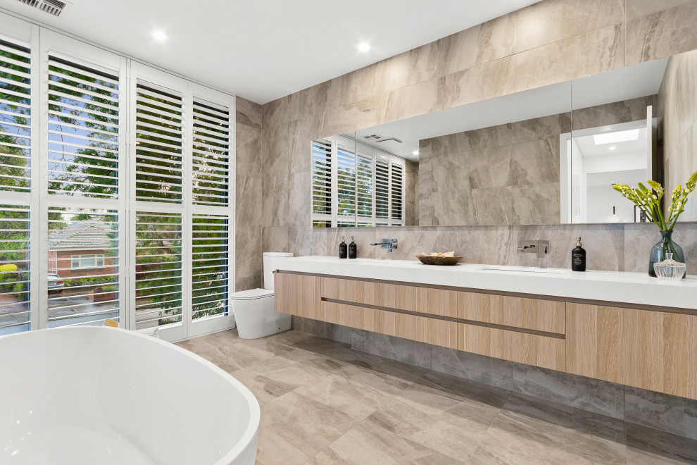 Design ideas for an expansive contemporary master bathroom in Melbourne with flat-panel cabinets, light wood cabinets, a freestanding tub, an open shower, a two-piece toilet, beige tile, beige walls, ceramic floors, an integrated sink, engineered quartz benchtops, beige floor, white benchtops, a double vanity and a floating vanity.