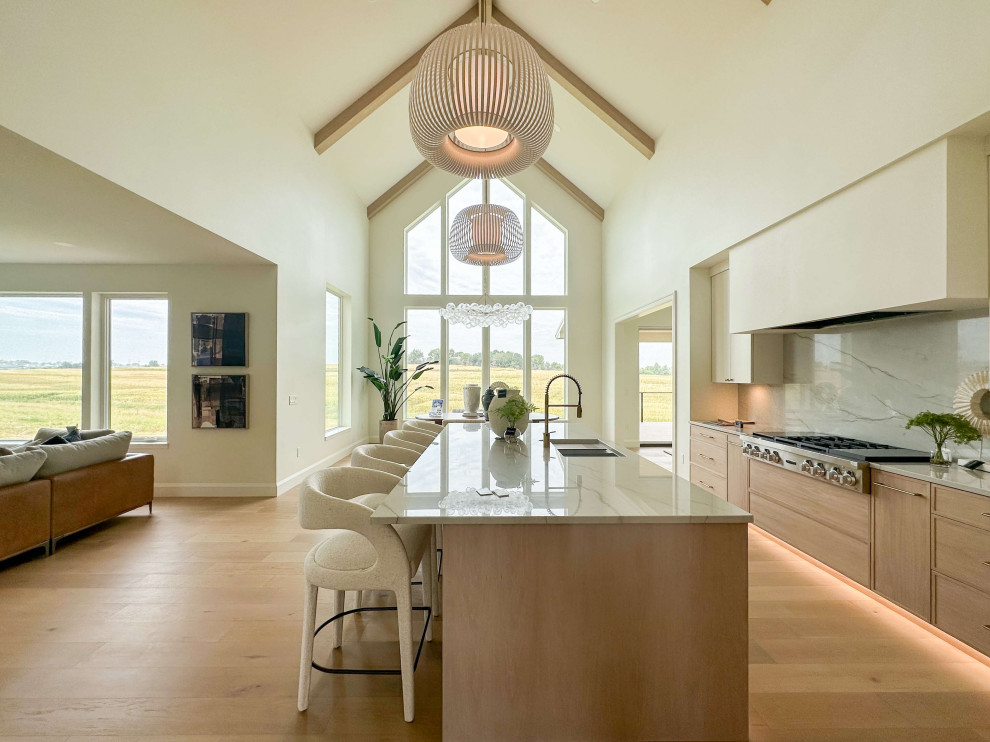 Example of a large transitional l-shaped light wood floor, beige floor and vaulted ceiling eat-in kitchen design with an undermount sink, shaker cabinets, light wood cabinets, quartzite countertops, white backsplash, stone slab backsplash, stainless steel appliances, an island and white countertops