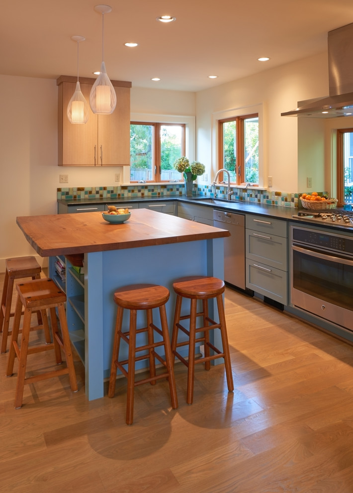 Inspiration for a mid-sized transitional l-shaped separate kitchen in Seattle with an undermount sink, shaker cabinets, blue cabinets, soapstone benchtops, multi-coloured splashback, glass tile splashback, stainless steel appliances, light hardwood floors, with island and beige floor.