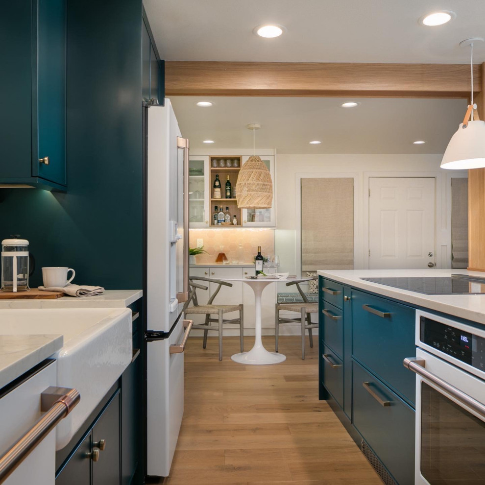 Mid-sized transitional single-wall light wood floor open concept kitchen photo in Seattle with a farmhouse sink, green cabinets, quartz countertops, beige backsplash, terra-cotta backsplash, white appliances, an island and white countertops