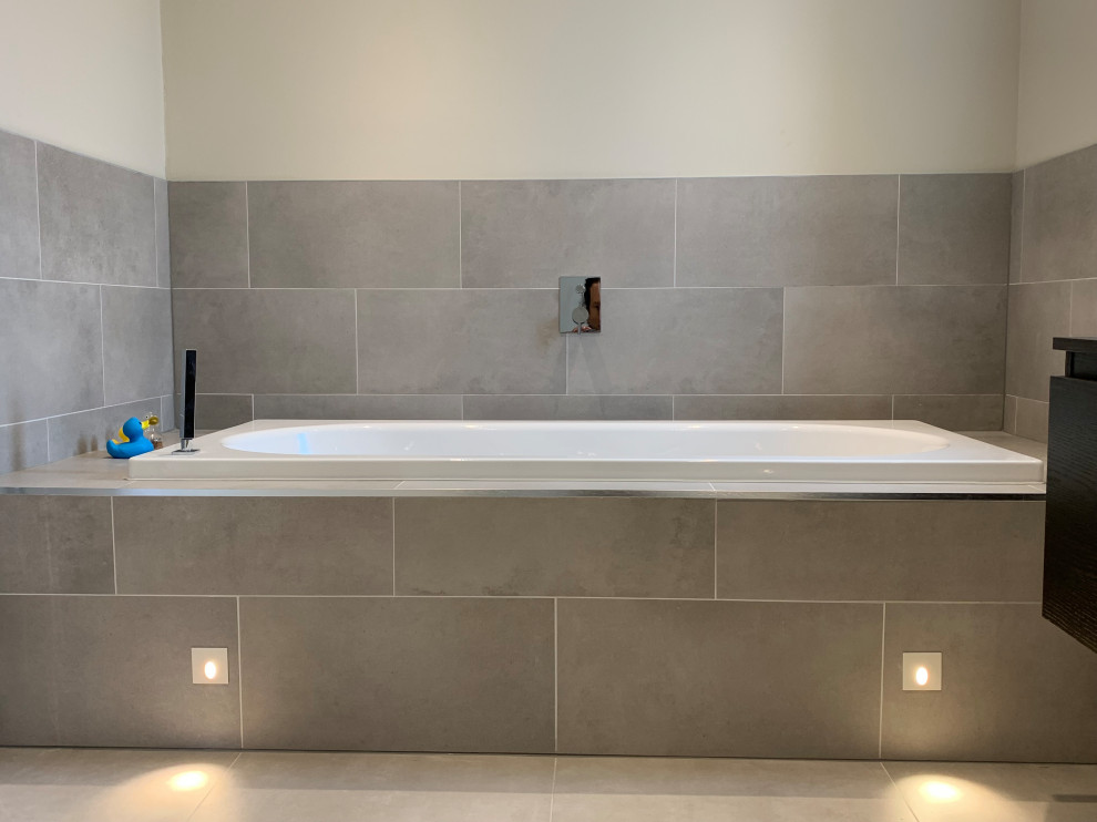 Photo of a large contemporary master bathroom in Surrey with flat-panel cabinets, dark wood cabinets, a drop-in tub, a curbless shower, a wall-mount toilet, gray tile, ceramic tile, grey walls, a vessel sink and a sliding shower screen.