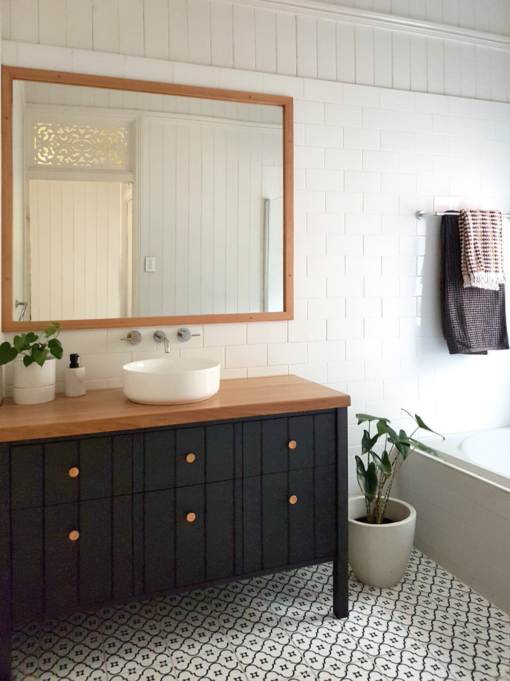 Exempel på ett mellanstort klassiskt brun brunt badrum, med luckor med lamellpanel, svarta skåp, ett platsbyggt badkar, en dusch/badkar-kombination, vit kakel, vita väggar, klinkergolv i keramik, ett fristående handfat, träbänkskiva, flerfärgat golv, dusch med gångjärnsdörr och keramikplattor
