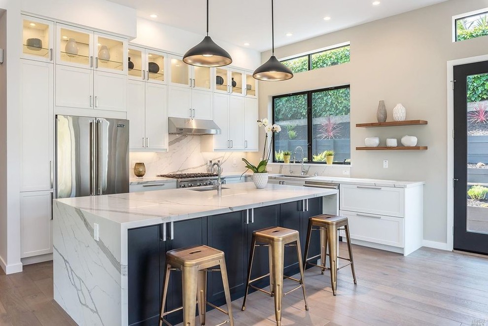Photo of a large contemporary u-shaped open plan kitchen in San Francisco with a drop-in sink, shaker cabinets, white cabinets, marble benchtops, white splashback, marble splashback, stainless steel appliances, medium hardwood floors and with island.
