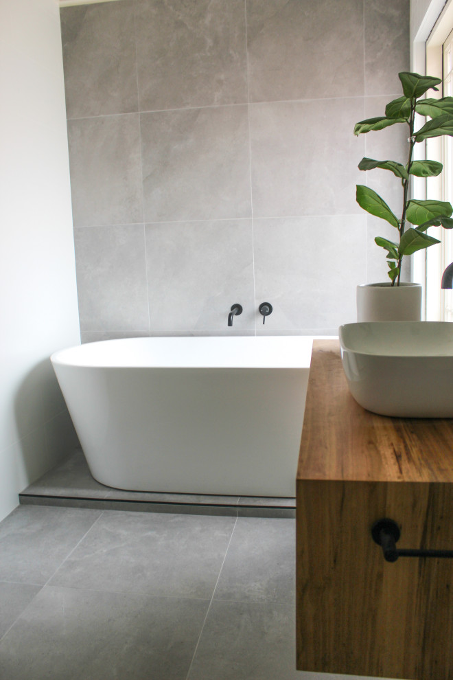 Photo of a large modern master bathroom in Perth with furniture-like cabinets, medium wood cabinets, a freestanding tub, a corner shower, a one-piece toilet, white tile, subway tile, white walls, porcelain floors, a vessel sink, wood benchtops, grey floor, a hinged shower door, multi-coloured benchtops, a single vanity and a floating vanity.