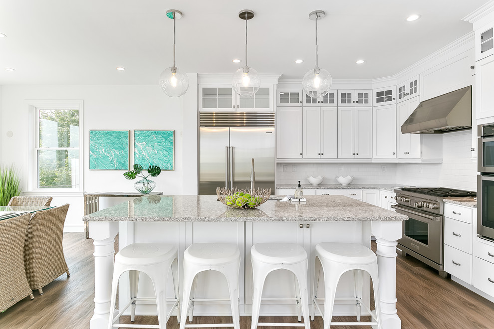 Photo of a large transitional l-shaped eat-in kitchen in Bridgeport with an undermount sink, glass-front cabinets, white cabinets, quartz benchtops, white splashback, ceramic splashback, stainless steel appliances, light hardwood floors, with island, brown floor and grey benchtop.