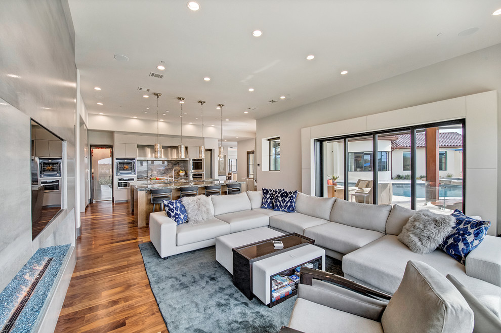 Photo of an expansive contemporary open concept family room in Orange County with white walls, medium hardwood floors, a standard fireplace, a stone fireplace surround, a built-in media wall and brown floor.