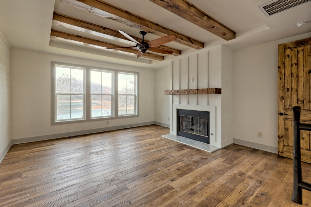 This is an example of a large country master bedroom in Atlanta with white walls, medium hardwood flooring, a standard fireplace, a wooden fireplace surround, brown floors and exposed beams.