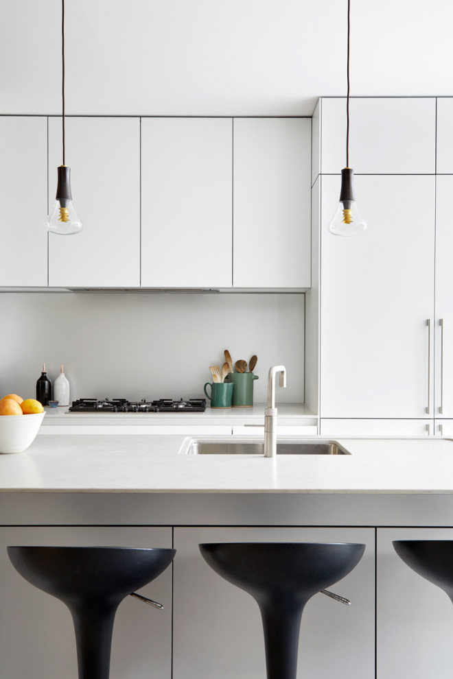 This is an example of a large contemporary galley open plan kitchen in London with a drop-in sink, flat-panel cabinets, white cabinets, marble benchtops, white splashback, granite splashback, panelled appliances, concrete floors, with island, grey floor and white benchtop.