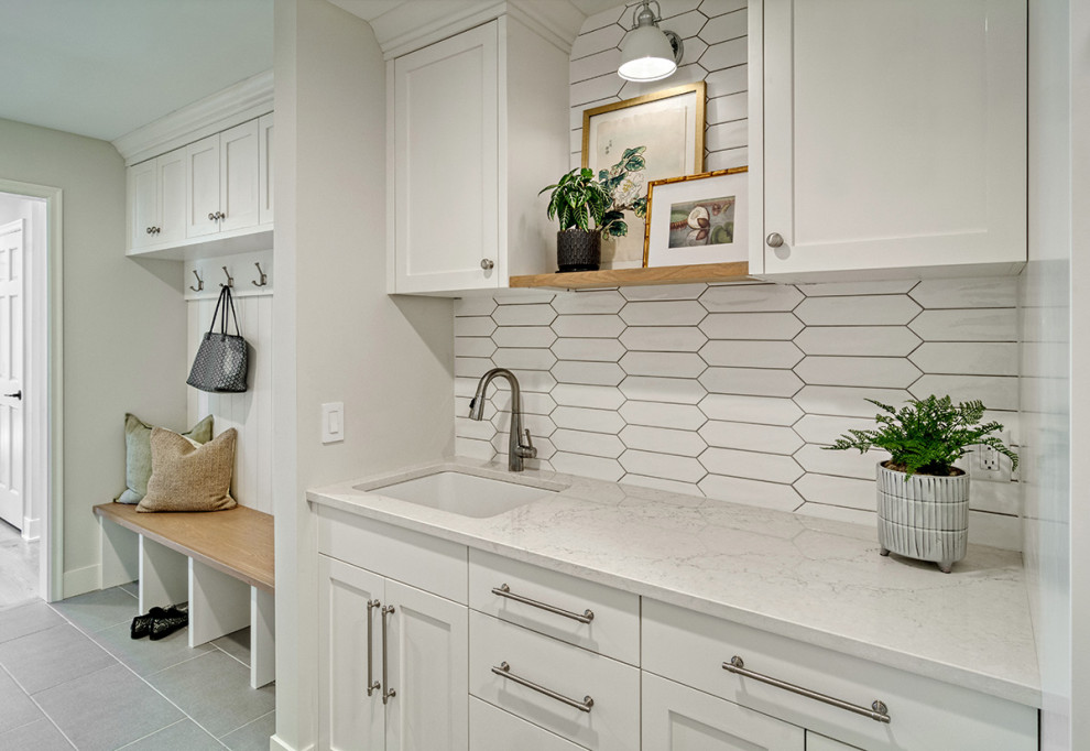 Inspiration for a small transitional galley utility room in Minneapolis with an undermount sink, flat-panel cabinets, distressed cabinets, quartzite benchtops, ceramic splashback, grey walls, ceramic floors, a stacked washer and dryer, grey floor, white benchtop and planked wall panelling.