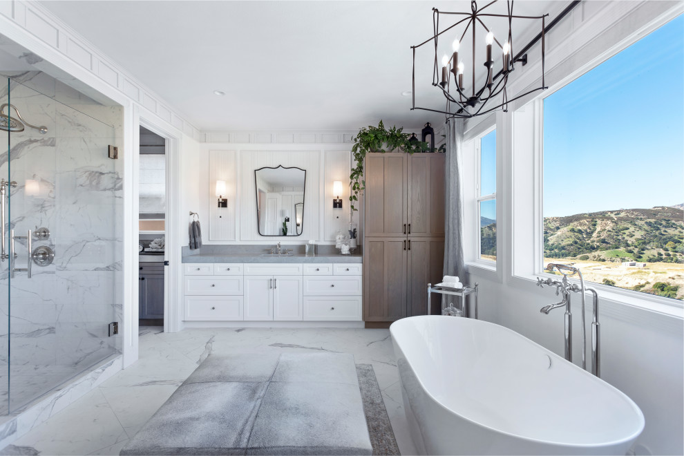 This is an example of a large classic ensuite bathroom in Los Angeles with shaker cabinets, white cabinets, a freestanding bath, a one-piece toilet, white tiles, porcelain tiles, white walls, porcelain flooring, a built-in sink, engineered stone worktops, white floors, a hinged door, grey worktops, a shower bench, double sinks, a built in vanity unit and wallpapered walls.