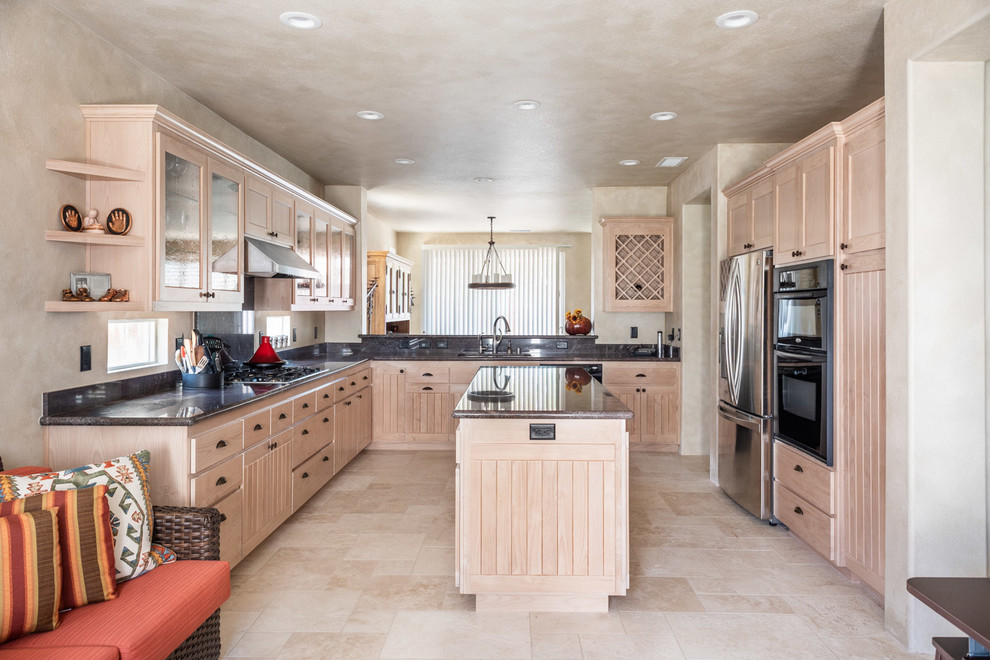 Photo of a mid-sized u-shaped eat-in kitchen in San Luis Obispo with recessed-panel cabinets, light wood cabinets, granite benchtops, limestone floors, with island, beige floor, black benchtop, an undermount sink, black splashback and stone slab splashback.