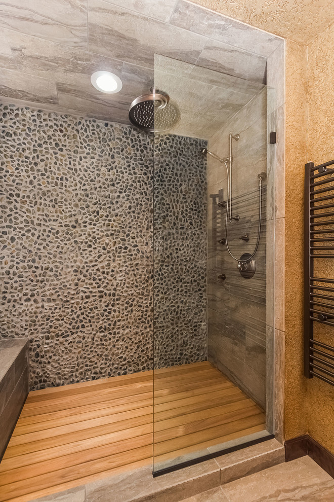 Photo of a mid-sized traditional bathroom in Minneapolis with recessed-panel cabinets, dark wood cabinets, an alcove shower, a two-piece toilet, gray tile, pebble tile, brown walls, porcelain floors, a vessel sink, limestone benchtops, beige floor, a hinged shower door and brown benchtops.