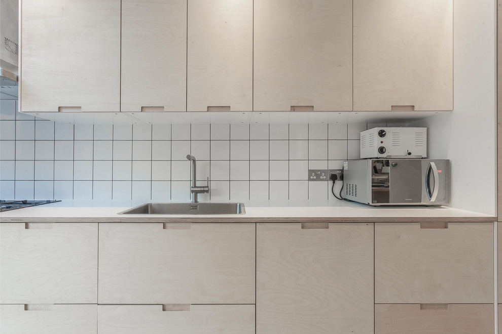 This is an example of a mid-sized scandinavian eat-in kitchen in London with an integrated sink, light wood cabinets, wood benchtops, white splashback, ceramic splashback, panelled appliances, ceramic floors, no island and grey floor.