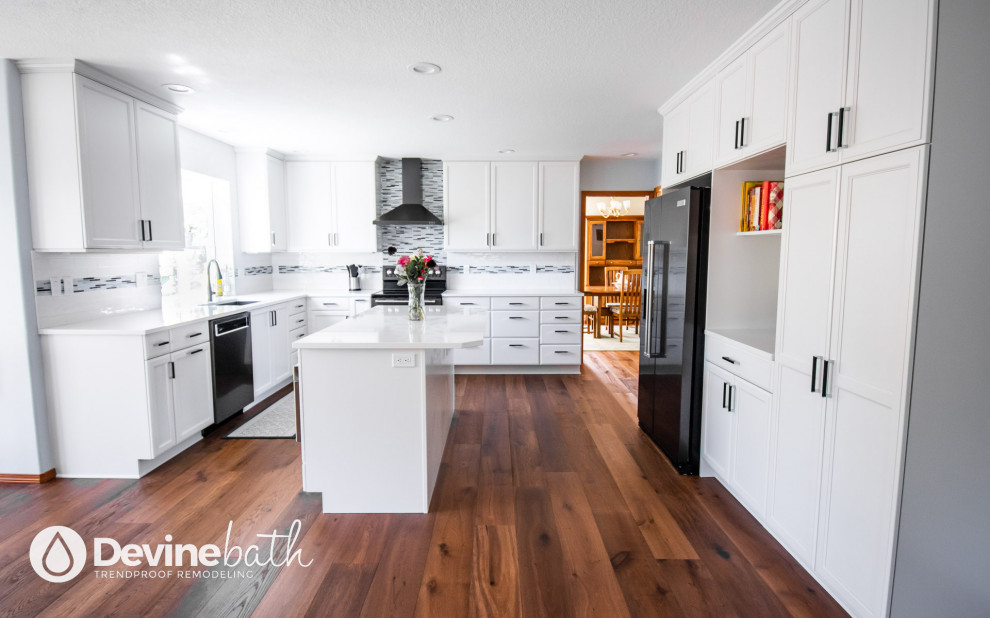 Example of a large transitional l-shaped medium tone wood floor open concept kitchen design in Portland with an undermount sink, recessed-panel cabinets, white cabinets, quartz countertops, white backsplash, glass tile backsplash, stainless steel appliances, an island and white countertops