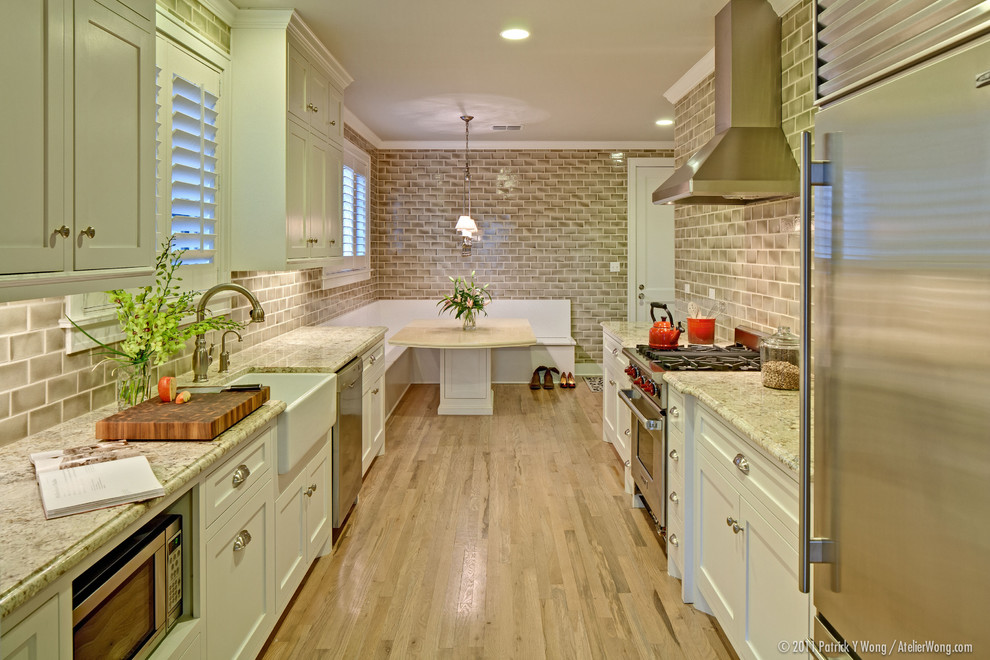 This is an example of a traditional galley separate kitchen in Austin with stainless steel appliances, granite benchtops, a farmhouse sink, recessed-panel cabinets, white cabinets, subway tile splashback and brown splashback.