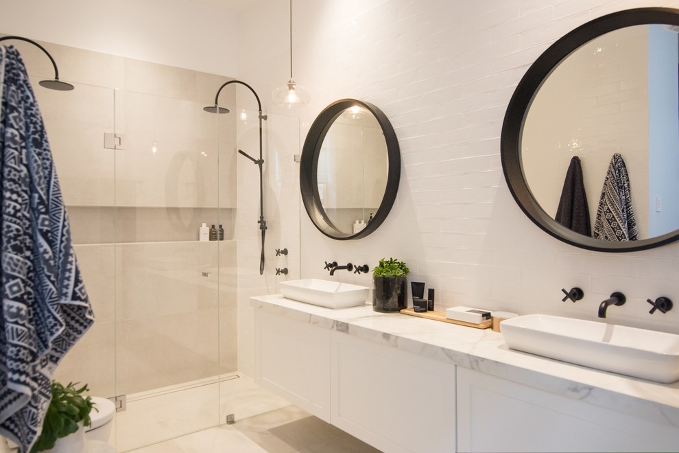 This is an example of a mid-sized contemporary master bathroom in Adelaide with recessed-panel cabinets, white cabinets, a double shower, a wall-mount toilet, white tile, subway tile, white walls, porcelain floors, a vessel sink, solid surface benchtops and grey floor.