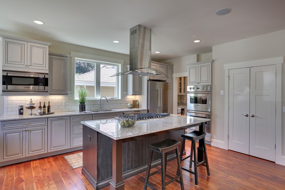 Mid-sized contemporary single-wall open plan kitchen in Minneapolis with a double-bowl sink, raised-panel cabinets, grey cabinets, granite benchtops, white splashback, subway tile splashback, stainless steel appliances, dark hardwood floors, with island and brown floor.