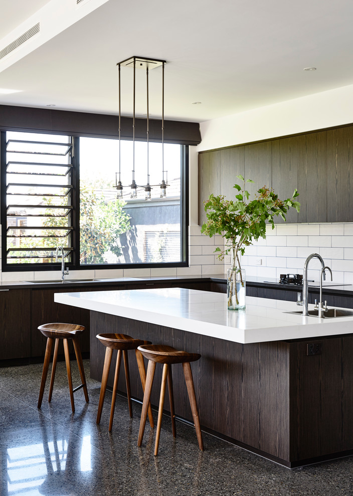 This is an example of a large contemporary l-shaped open plan kitchen in Melbourne with a double-bowl sink, flat-panel cabinets, dark wood cabinets, solid surface benchtops, white splashback, ceramic splashback, stainless steel appliances, concrete floors and with island.