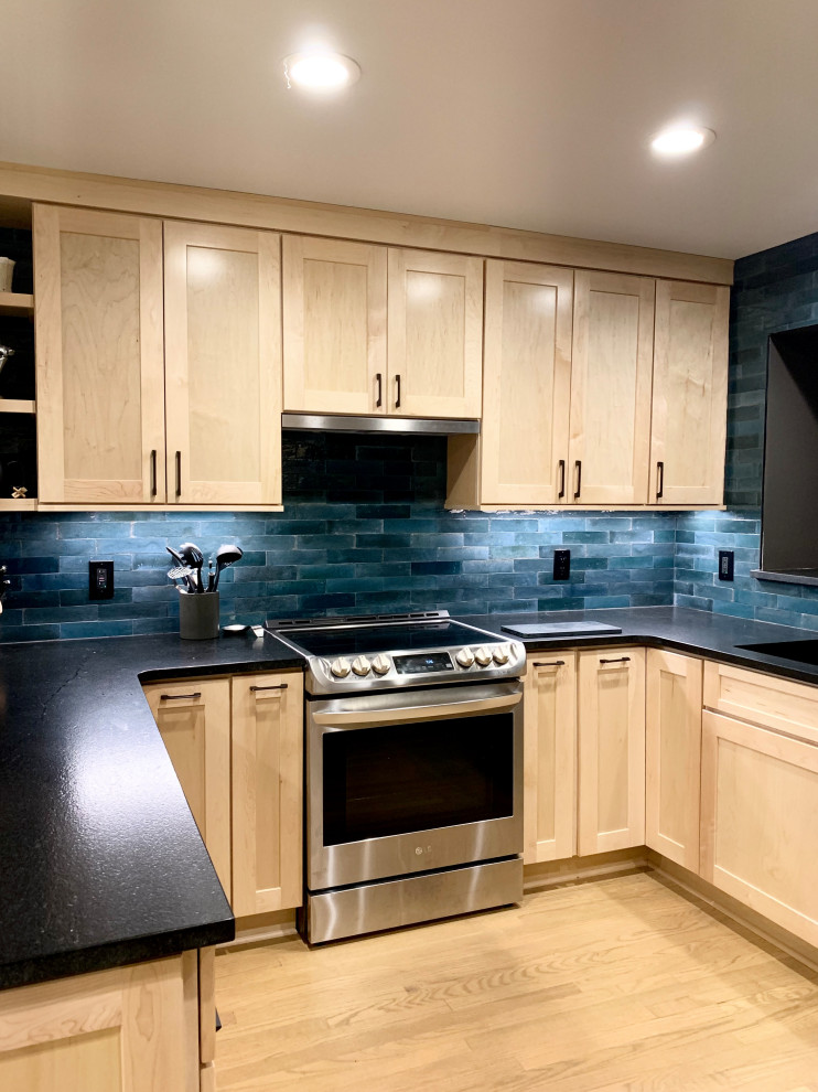 Mid-sized transitional u-shaped eat-in kitchen in Other with an undermount sink, shaker cabinets, light wood cabinets, granite benchtops, blue splashback, ceramic splashback, stainless steel appliances, light hardwood floors, a peninsula, brown floor and black benchtop.