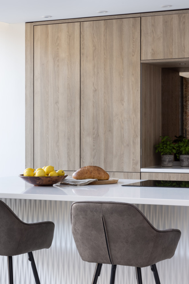 Idée de décoration pour une cuisine américaine nordique en bois brun de taille moyenne avec un placard à porte plane, un plan de travail en surface solide, une crédence miroir, un électroménager noir, îlot et un plan de travail blanc.