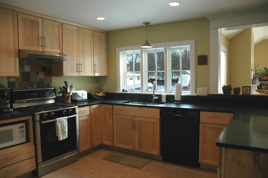 Photo of a mid-sized contemporary u-shaped eat-in kitchen in Burlington with a double-bowl sink, shaker cabinets, light wood cabinets, black appliances, porcelain floors, a peninsula and solid surface benchtops.