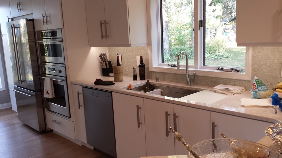 Inspiration for a small transitional galley medium tone wood floor enclosed kitchen remodel with an undermount sink, flat-panel cabinets, white cabinets, quartz countertops, white backsplash, mosaic tile backsplash, stainless steel appliances and a peninsula