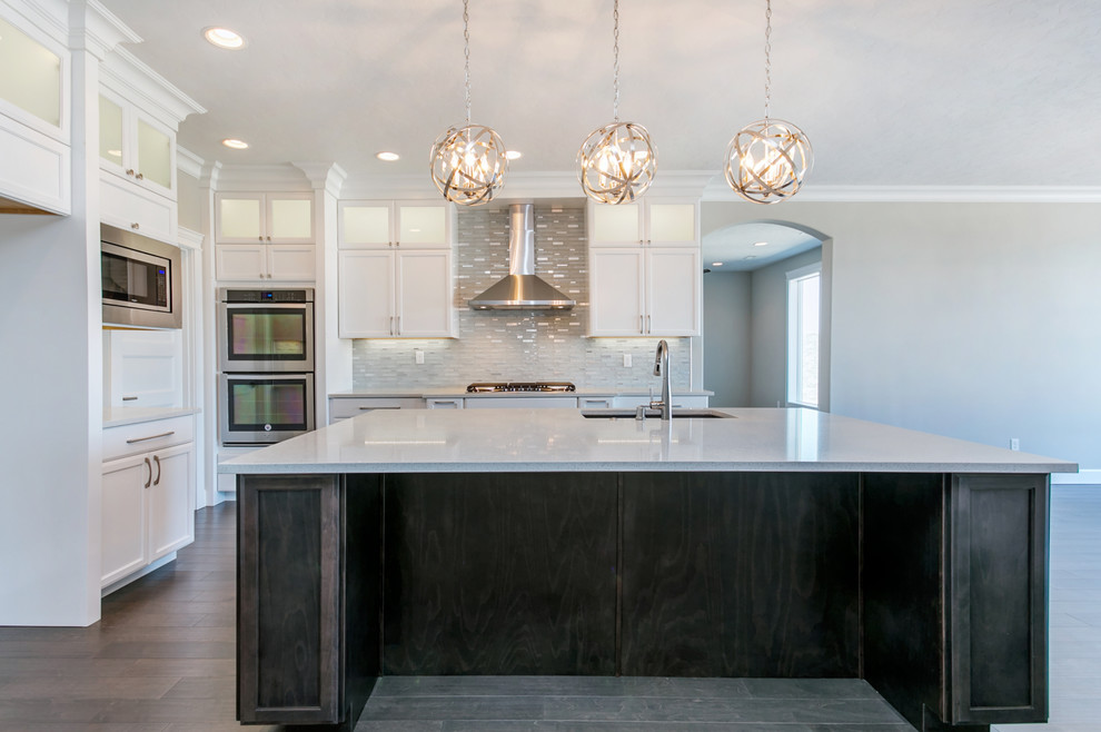Example of a mid-sized transitional l-shaped medium tone wood floor open concept kitchen design in Seattle with an undermount sink, recessed-panel cabinets, white cabinets, quartz countertops, white backsplash, glass tile backsplash, stainless steel appliances, an island and white countertops