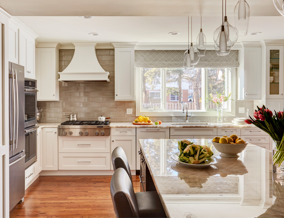 Inspiration for a transitional l-shaped kitchen in Chicago with an undermount sink, recessed-panel cabinets, white cabinets, beige splashback, subway tile splashback, stainless steel appliances, medium hardwood floors, with island, brown floor and beige benchtop.
