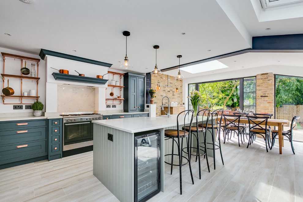Inspiration for a large transitional single-wall eat-in kitchen in London with blue cabinets, beige splashback, stainless steel appliances, with island, shaker cabinets, beige floor and beige benchtop.