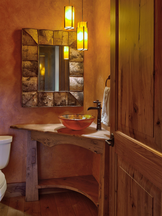 Design ideas for a mid-sized country powder room in Denver with open cabinets, orange walls, medium hardwood floors, a vessel sink, wood benchtops, brown floor, brown benchtops, a freestanding vanity and wallpaper.