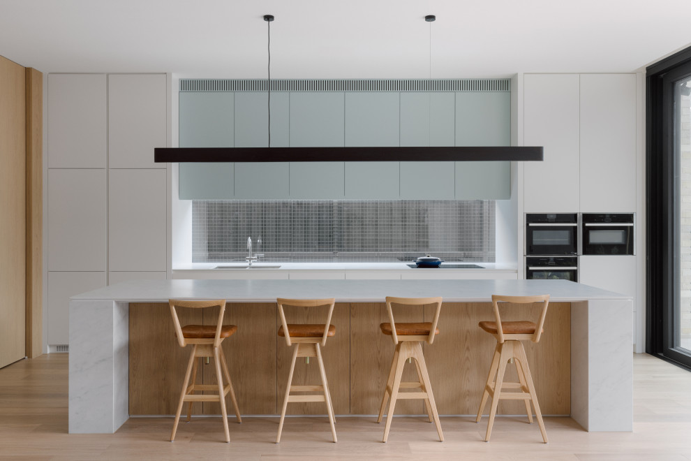 Photo of a modern galley kitchen in Melbourne with an undermount sink, flat-panel cabinets, blue cabinets, black appliances, with island, beige floor and white benchtop.