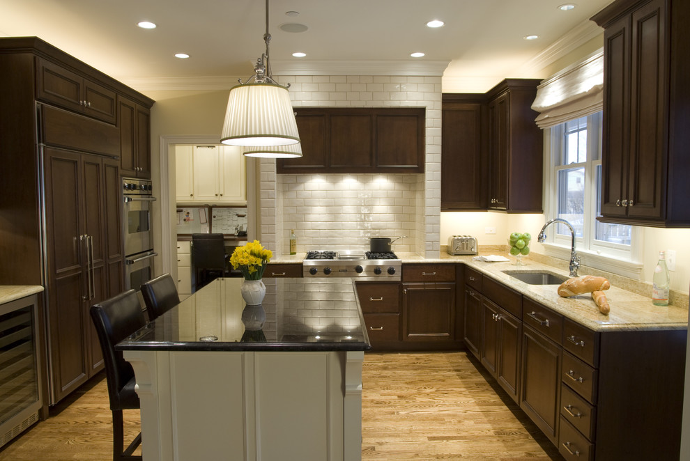 Design ideas for a traditional u-shaped kitchen in Chicago with subway tile splashback, an undermount sink, recessed-panel cabinets, dark wood cabinets, granite benchtops, white splashback and panelled appliances.