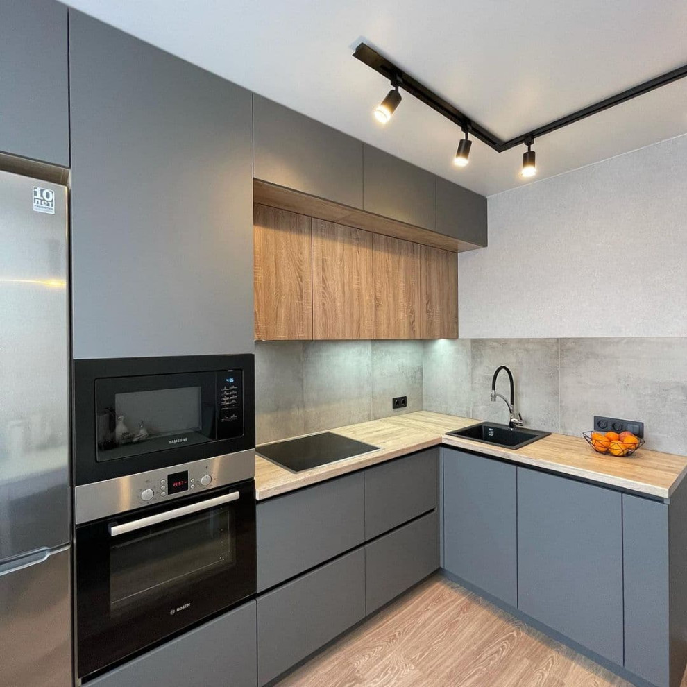 Mid-sized contemporary l-shaped eat-in kitchen in Moscow with a drop-in sink, flat-panel cabinets, green cabinets, wood benchtops, grey splashback, porcelain splashback, black appliances, laminate floors, no island, brown floor and yellow benchtop.