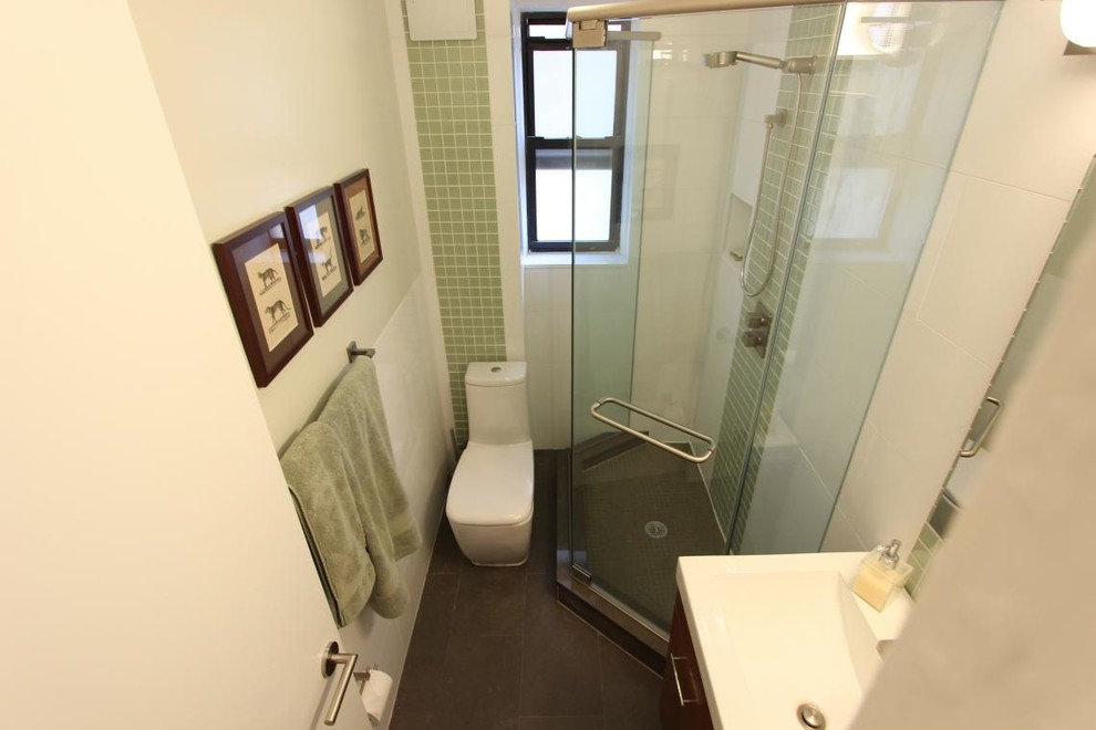 Photo of a small eclectic 3/4 bathroom in New York with a wall-mount sink, flat-panel cabinets, medium wood cabinets, a corner shower, a one-piece toilet, green tile, glass tile, white walls, porcelain floors and solid surface benchtops.