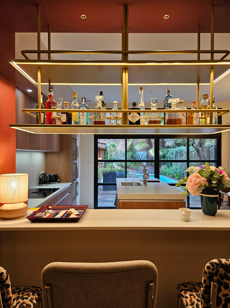 This is an example of a large midcentury l-shaped seated home bar in Bordeaux with an integrated sink, beaded inset cabinets, medium wood cabinets, quartz benchtops, beige splashback and beige benchtop.