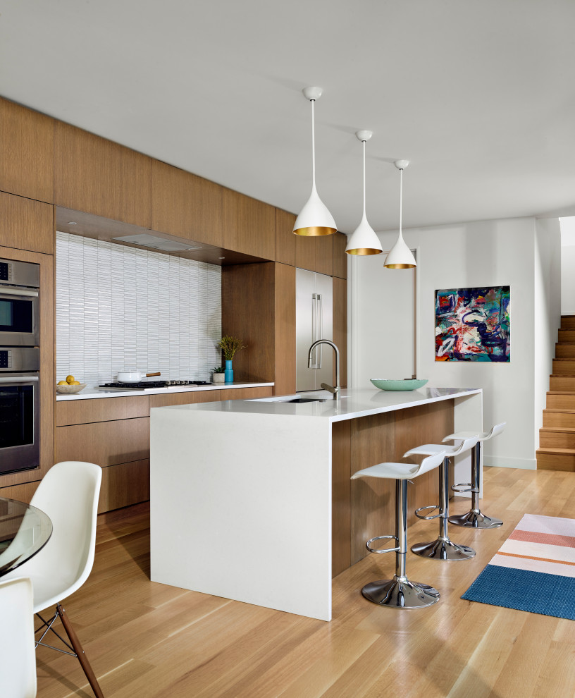 Photo of a large contemporary galley eat-in kitchen in Austin with flat-panel cabinets, quartz benchtops, white splashback, stainless steel appliances, medium hardwood floors, with island, brown floor, white benchtop, an undermount sink and medium wood cabinets.