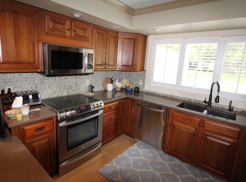 Inspiration for a transitional medium tone wood floor and brown floor kitchen remodel with an undermount sink, raised-panel cabinets, dark wood cabinets, quartz countertops, multicolored backsplash, stainless steel appliances and brown countertops