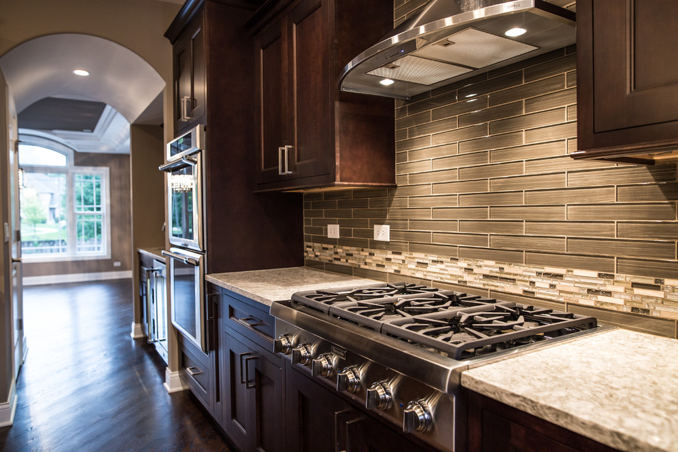Example of a mid-sized transitional l-shaped dark wood floor eat-in kitchen design in Chicago with an undermount sink, shaker cabinets, brown cabinets, granite countertops, gray backsplash, subway tile backsplash, stainless steel appliances and an island